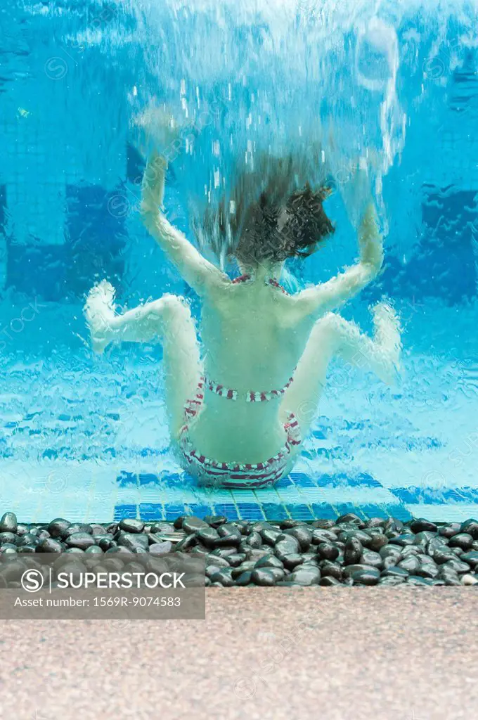 Girl swimming underwater in swimming pool, rear view