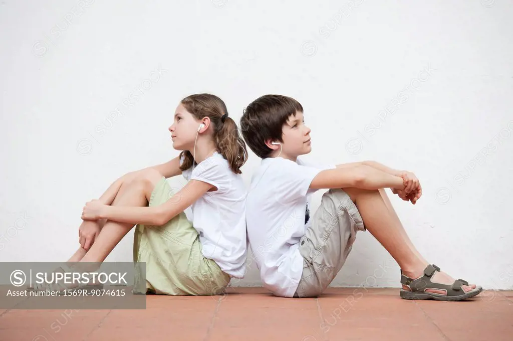 Boy and girl sitting back to back listening to music together