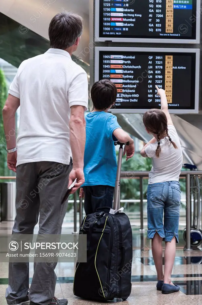 Family looking at arrival departure board, rear view