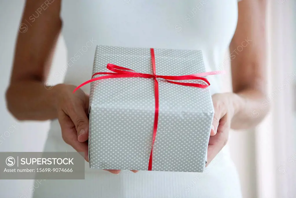 Woman holding out wrapped gift, cropped