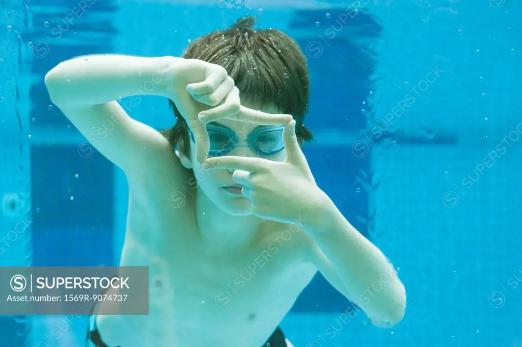 Boy swimming underwater in swimming pool, hands forming finger frame