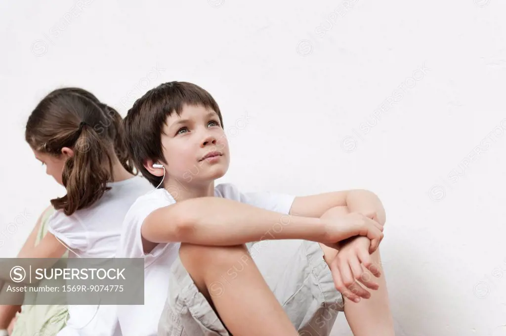 Boy and girl sitting back to back listening to music with earphones
