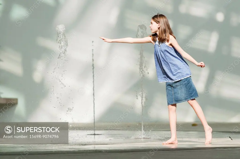 Girl reaching for vertical water jet rising from public fountain