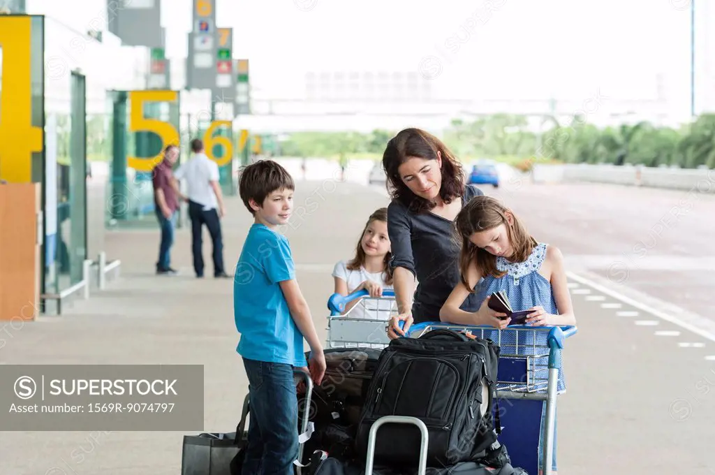Family standing outside of airport with luggage