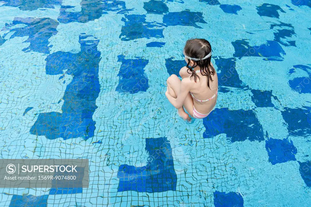 Girl jumping into swimming pool, rear view