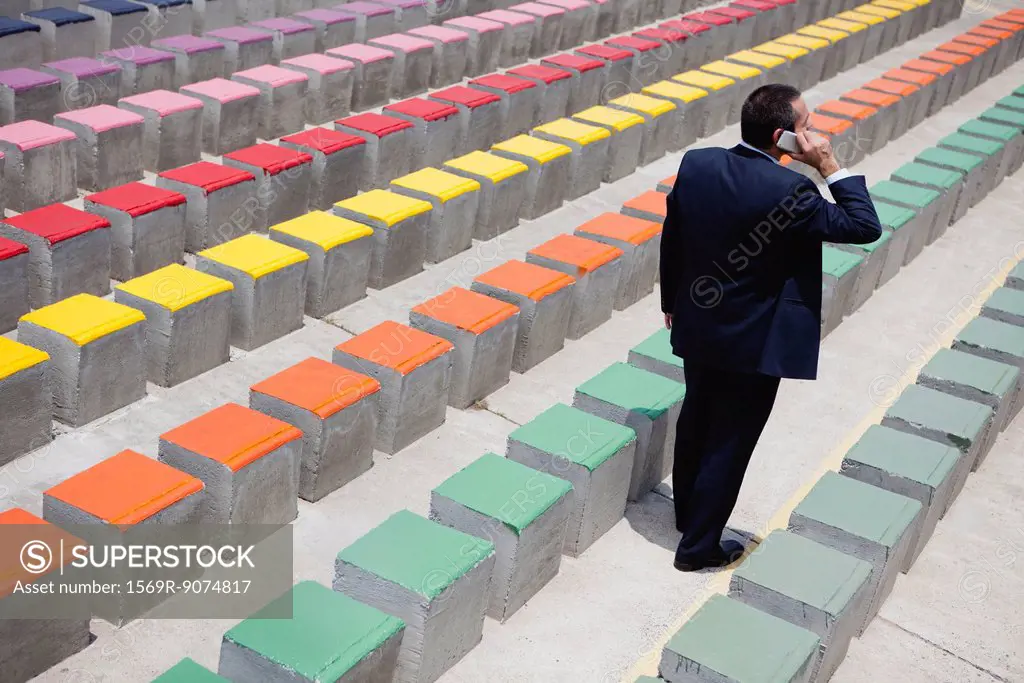 Business executive using cell phone by rows of bleachers, rear view