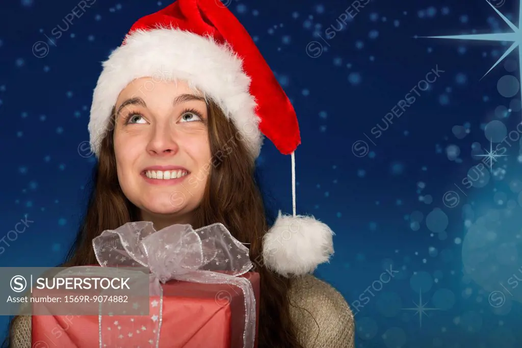 Young woman wearing Santa hat, holding Christmas present, portrait