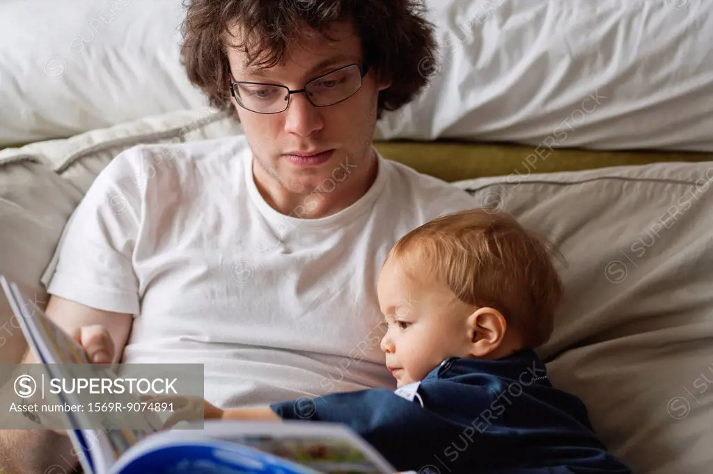 Young man reading book to baby boy