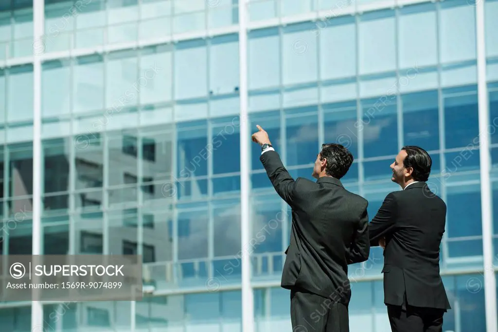 Business executives standing in front of office building, one pointing into distance