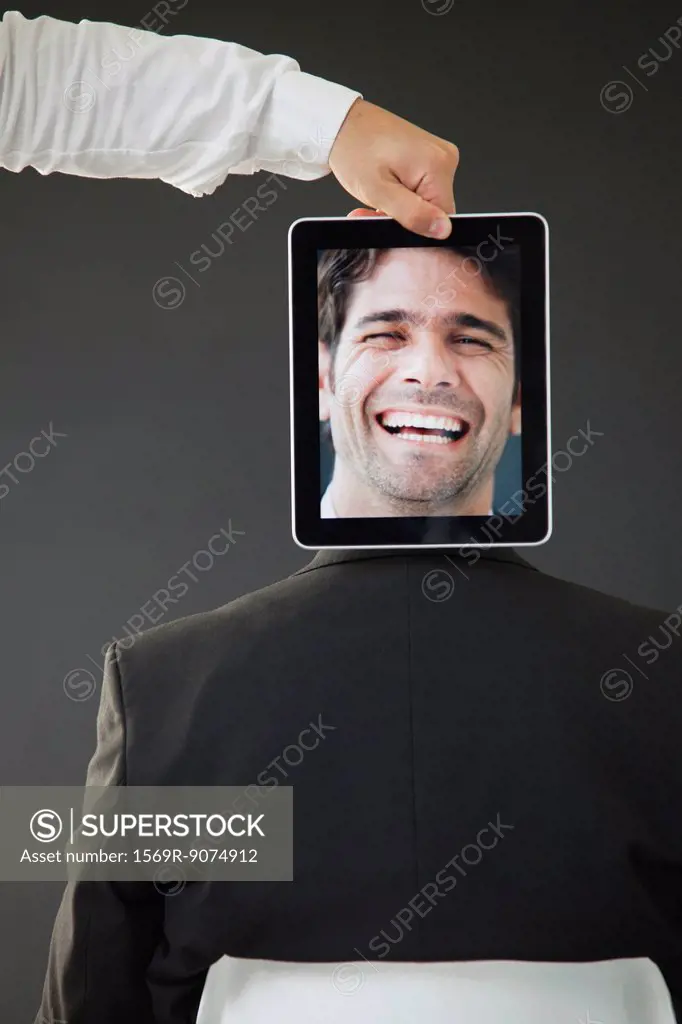Man concealed behind digital tablet displaying image of laughing man, rear view