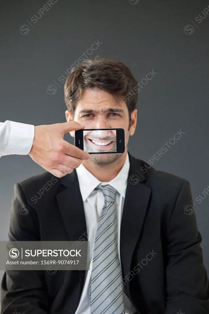 Man with mouth concealed behind smartphone displaying image of his own smile