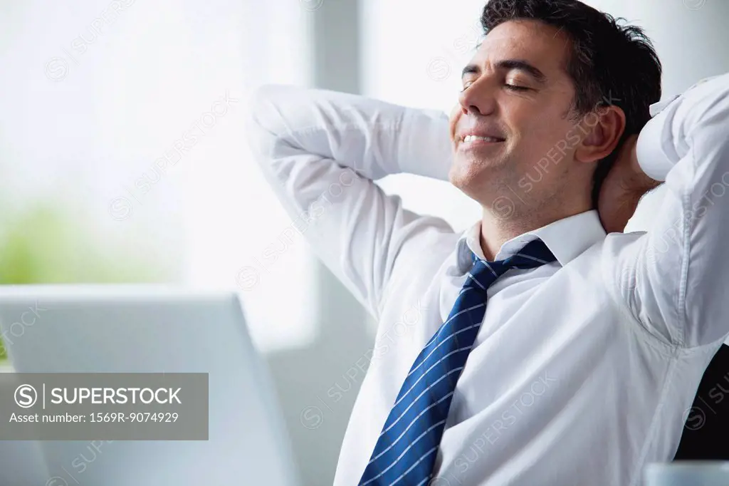 Businessman relaxing at desk hands behind head