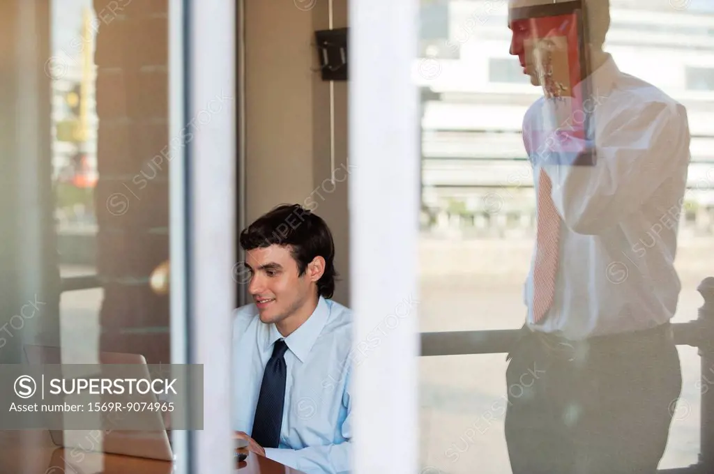 Businessman in office seen from outside of window, reflection of man using cell phone outdoors
