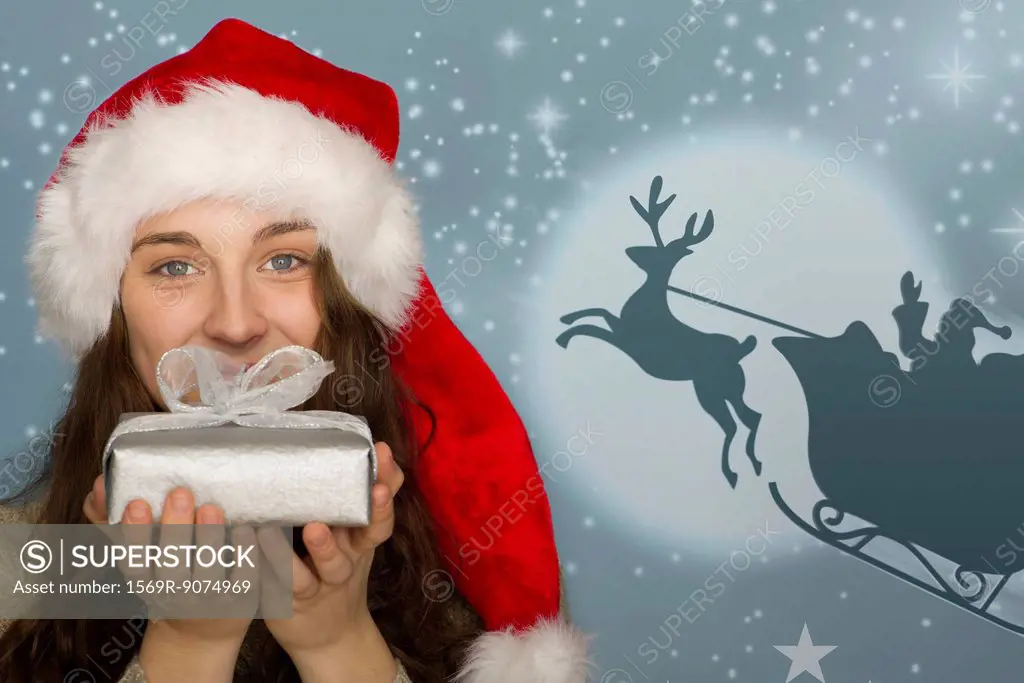 Young woman in Santa hat holding Christmas present, graphic of Santa´s sleigh in background