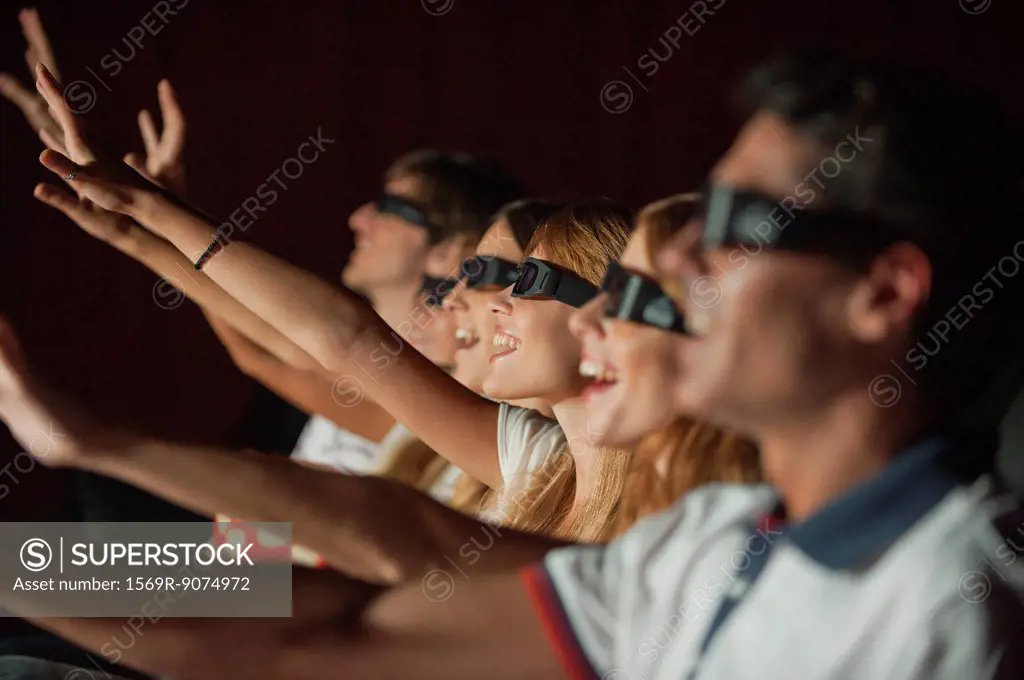 Audience wearing 3_D glasses in movie theater, arms reaching out