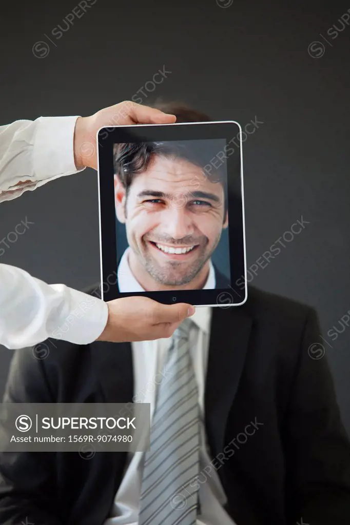 Man concealed behind digital tablet displaying image of smiling man