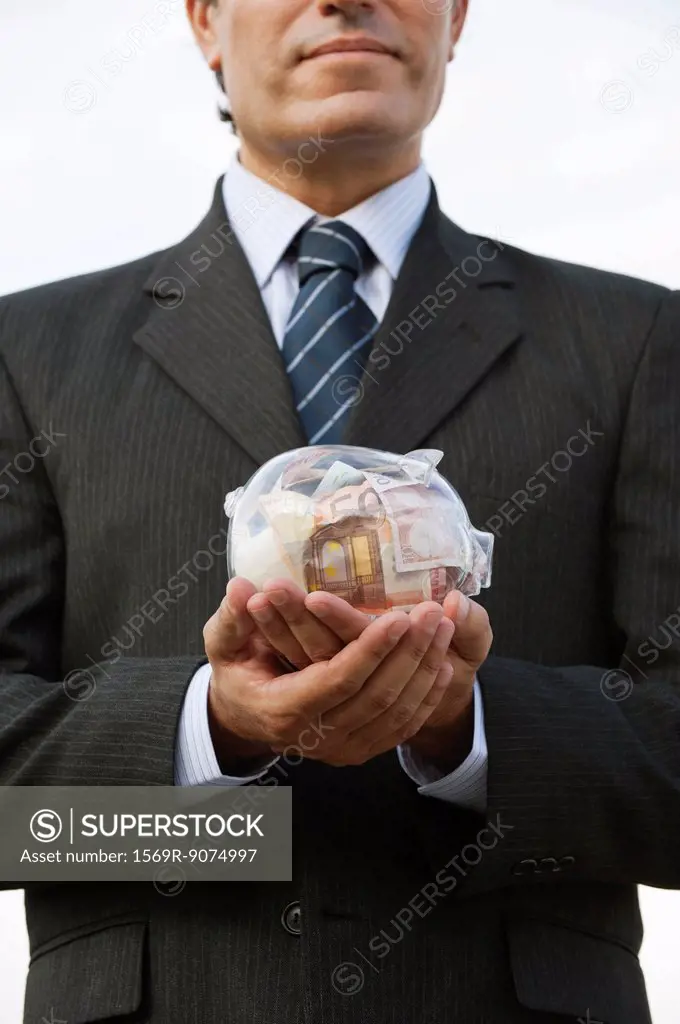 Man holding transparent piggy bank filled with euros