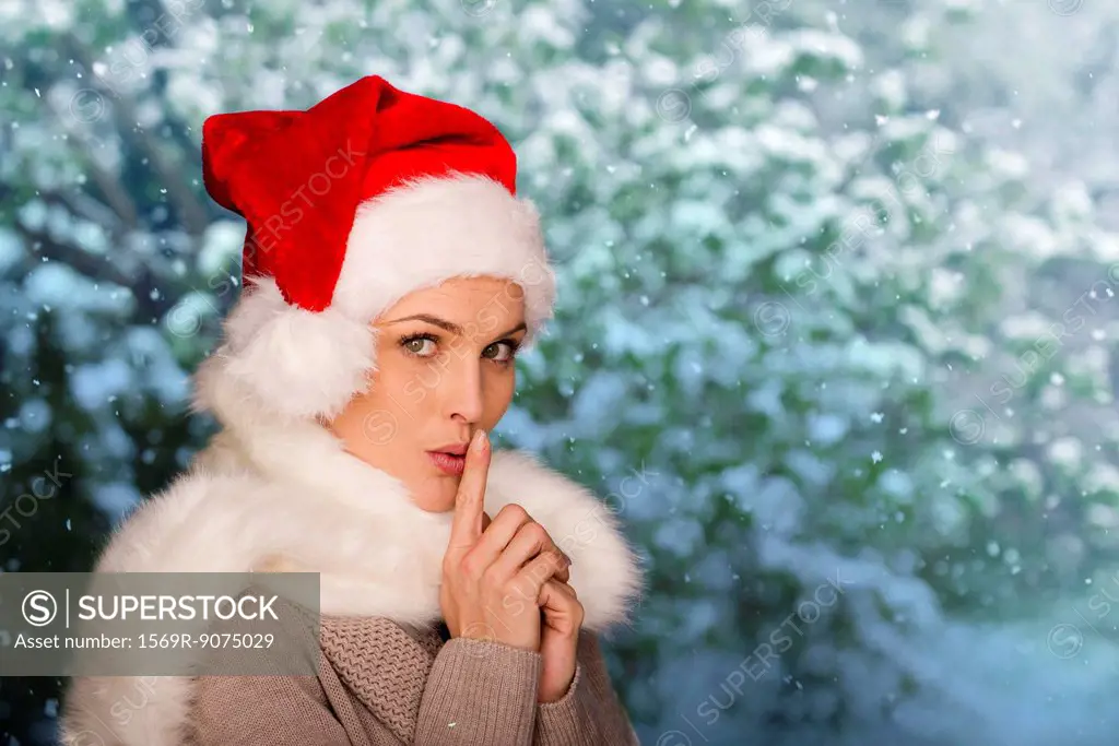 Woman wearing Santa hat, finger on lips, portrait