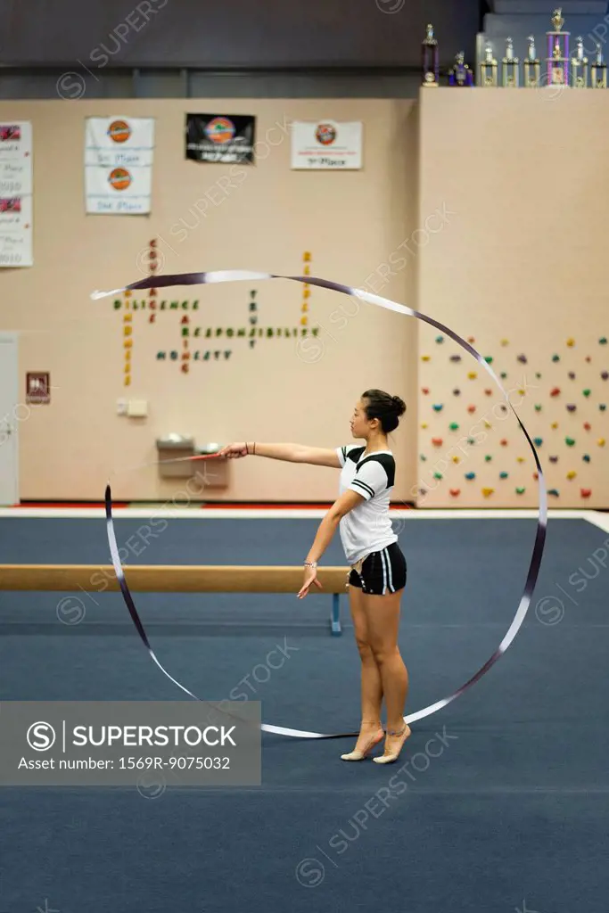 Teenage girl gymnast practicing rhythmic gymnastics, twirling ribbon