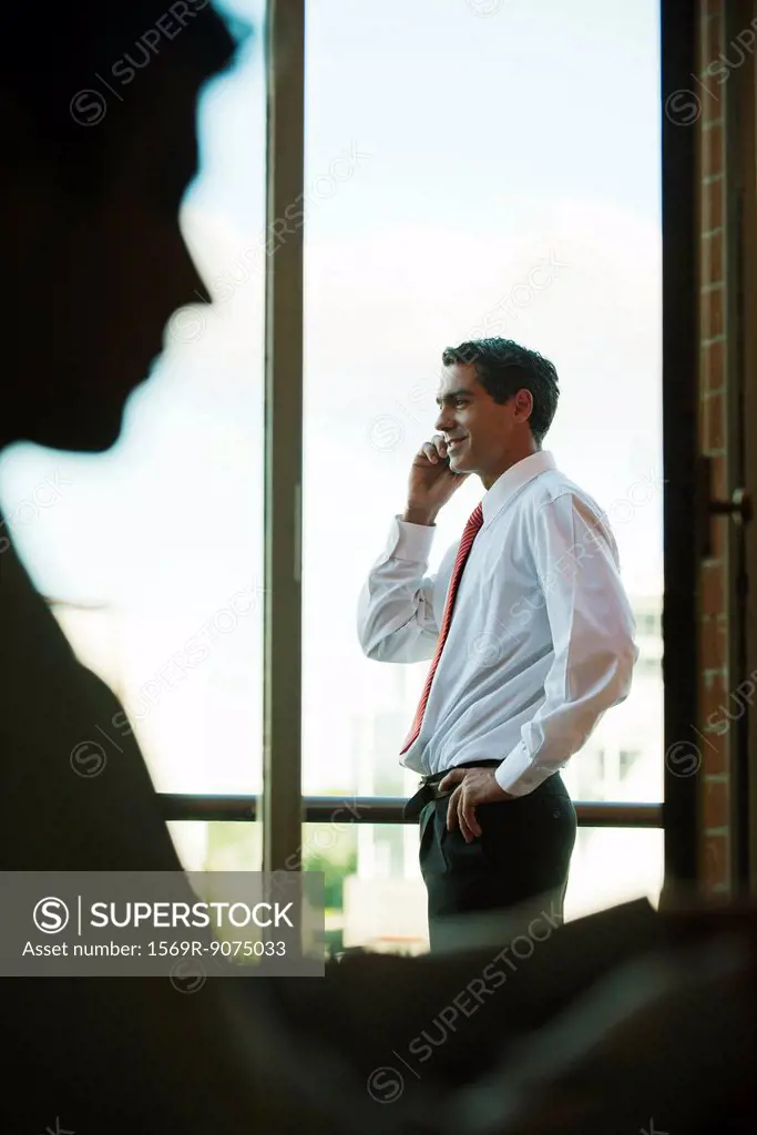 Silhouette of businessman using cell phone by window