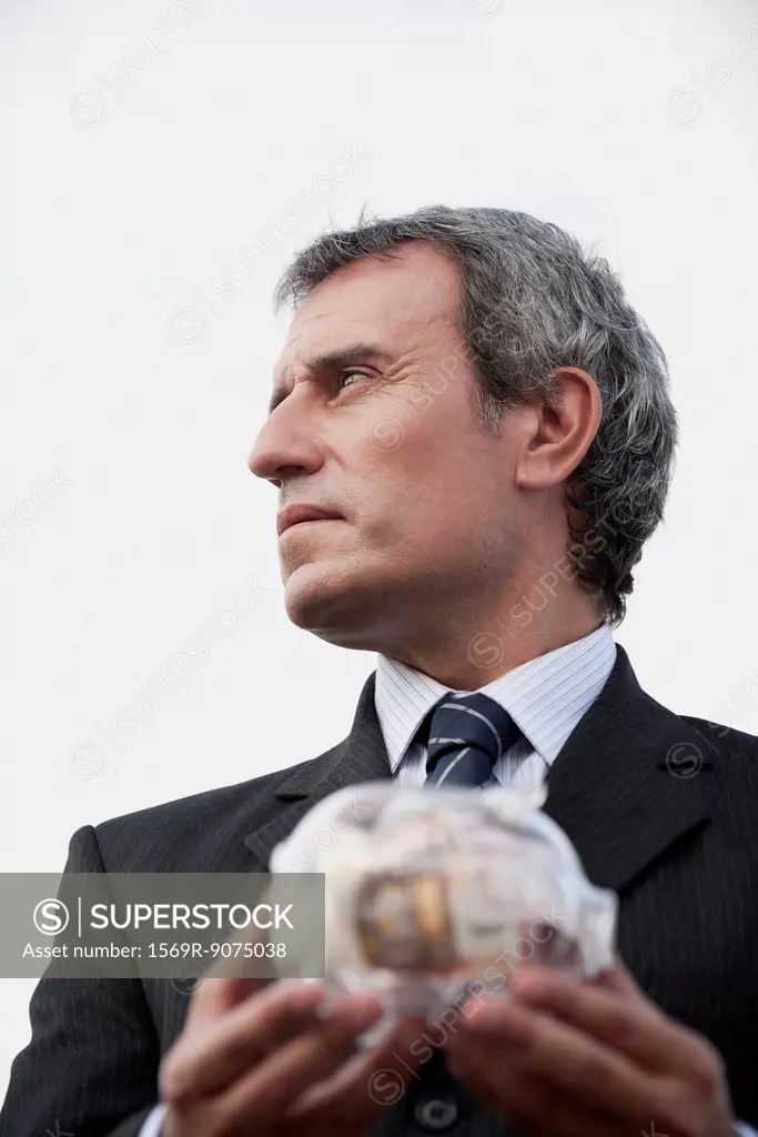 Mature man holding transparent piggy bank filled with euros
