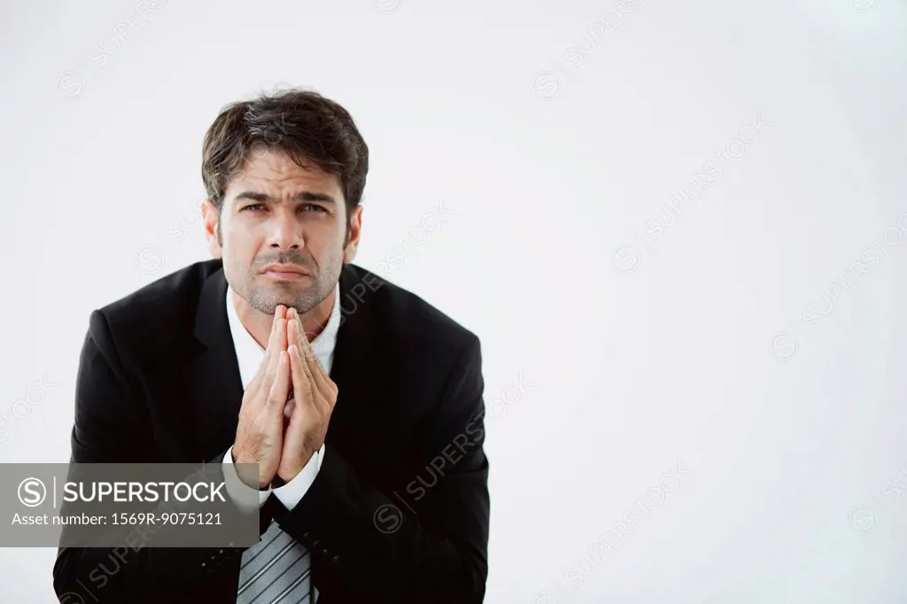 Businessman with hands clasped under chin, disappointed expression on face