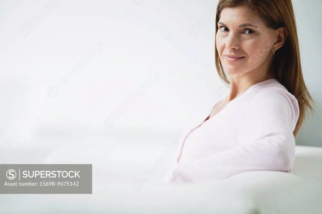 Mature woman sitting on couch, smiling over shoulder
