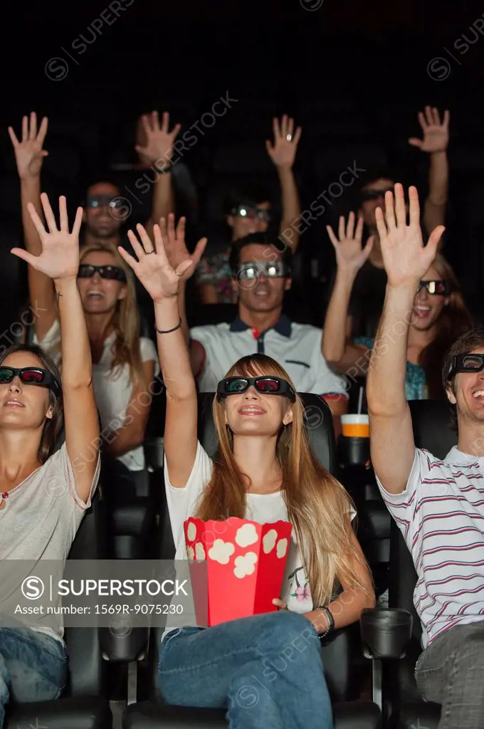 Audience wearing 3_D glasses in movie theater, arms reaching up
