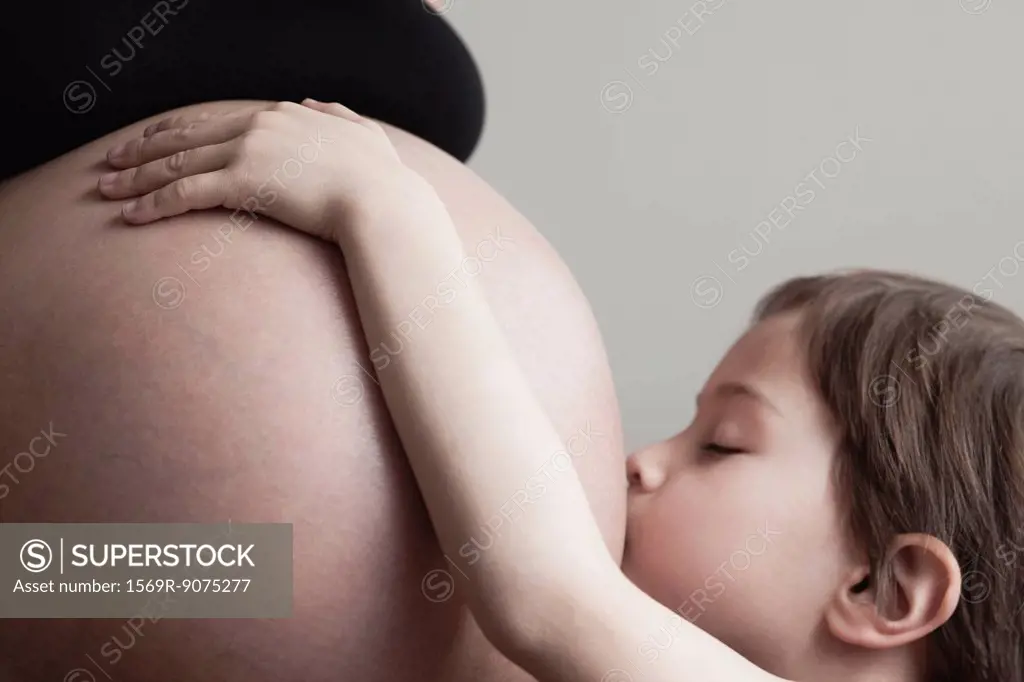 Boy kissing pregnant mother´s stomach, cropped
