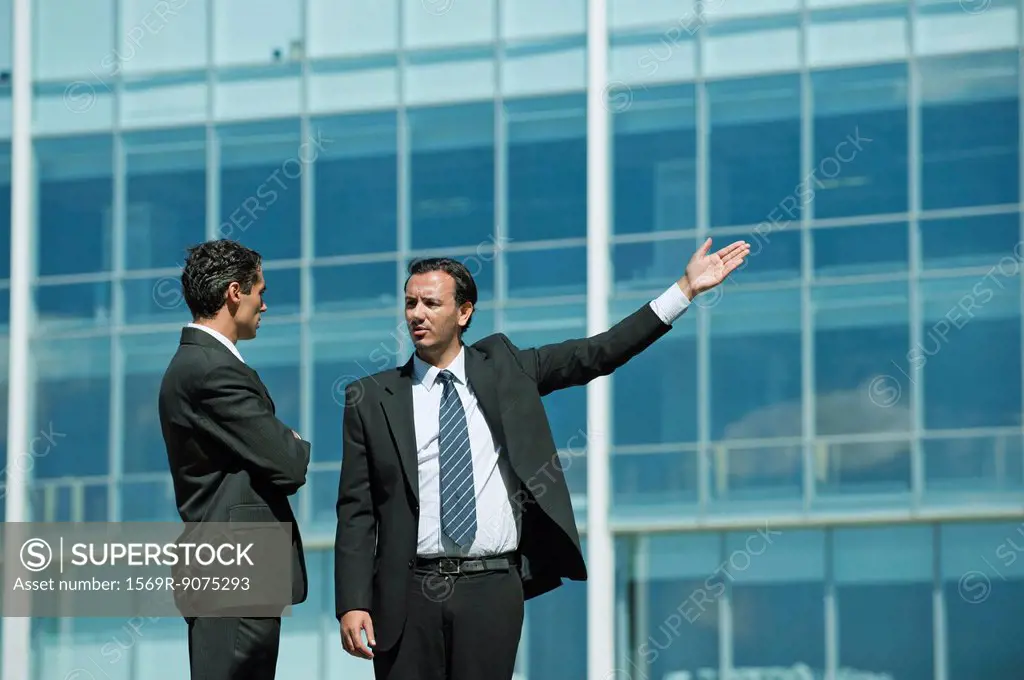 Business executives standing in front of office building, one pointing into distance