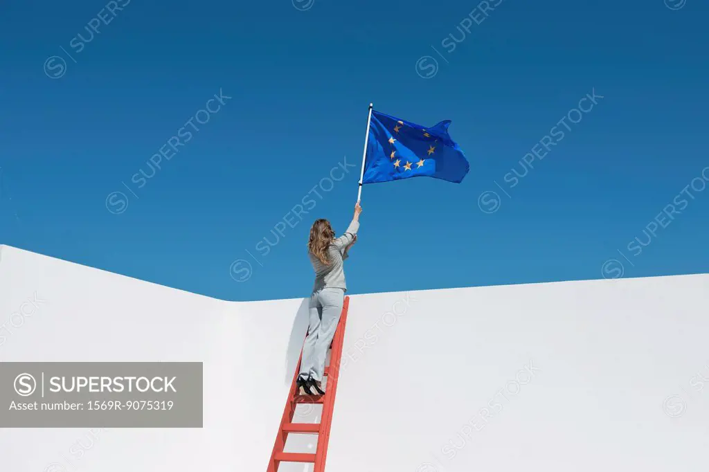 Businesswoman standing at top of ladder, holding European Union flag