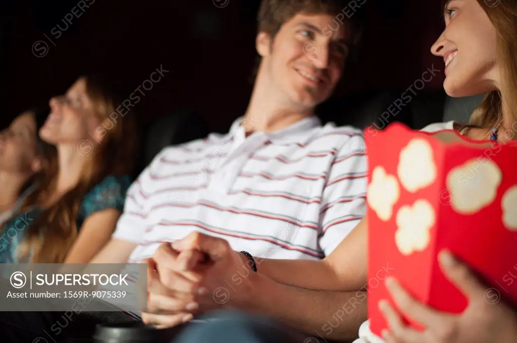 Couple looking at each other and holding hands in movie theater