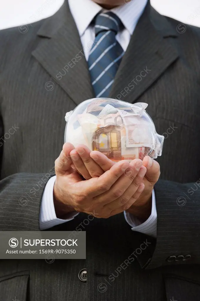 Man holding transparent piggy bank filled with euros, cropped