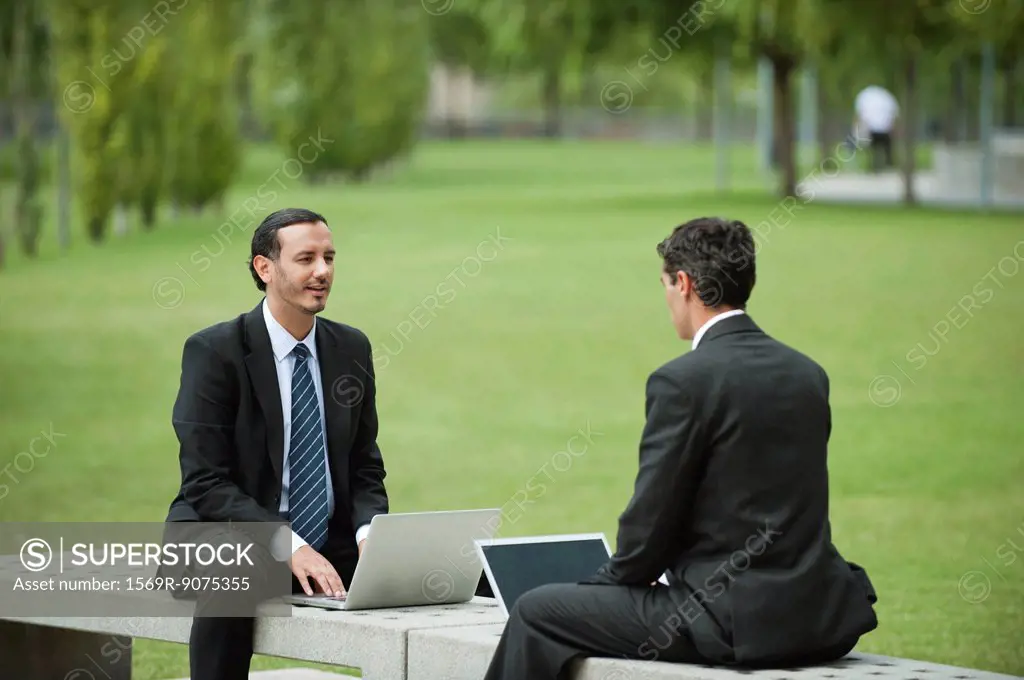 Business executives discussing work while using laptop computers outdoors