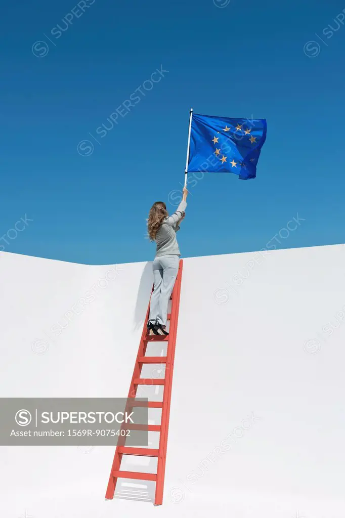 Businesswoman standing at top of ladder, holding European Union flag