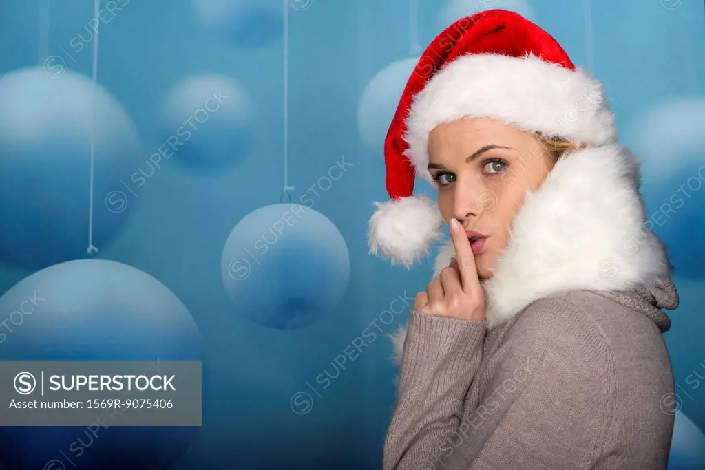 Woman wearing Santa hat, finger on lips, portrait