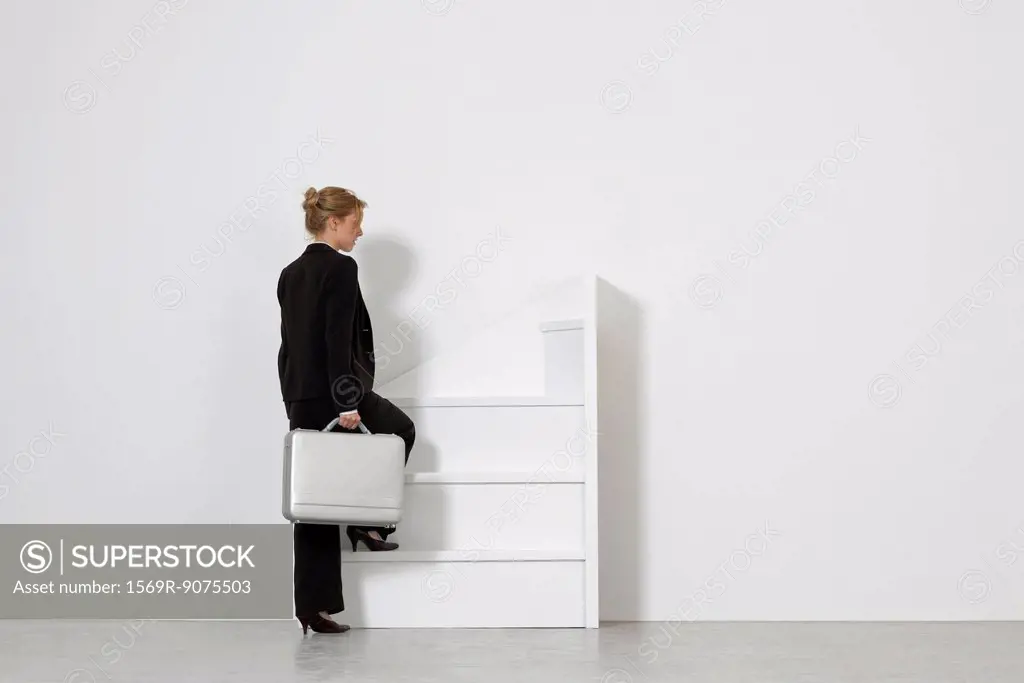 Businesswoman walking up incomplete staircase, rear view