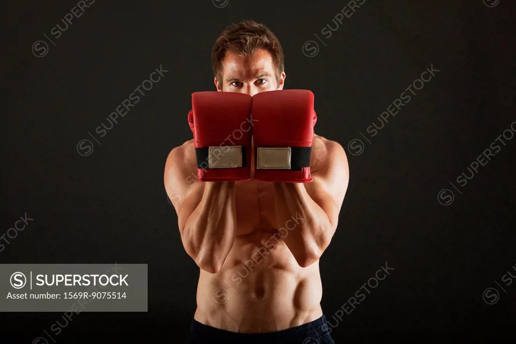 Barechested boxer holding up gloves in front of face in defensive position
