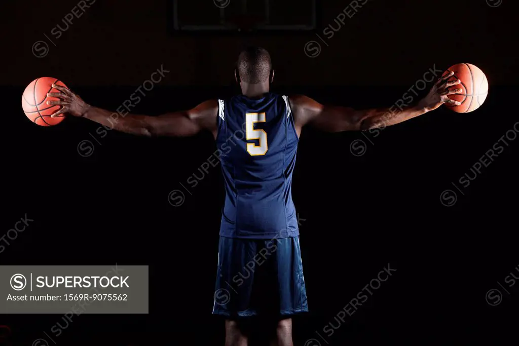 Basketball player holding basketballs in both hands, rear view