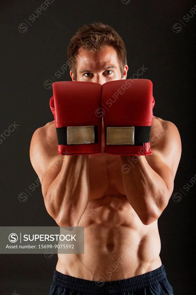 Barechested boxer holding up gloves in front of face in defensive position
