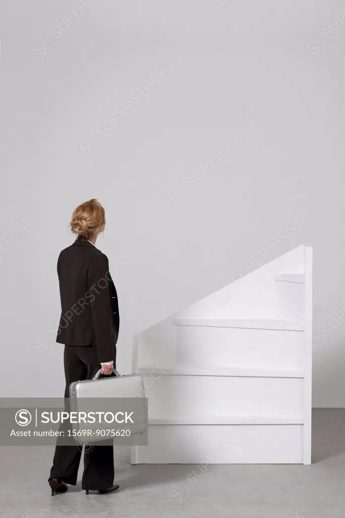 Businesswoman standing before incomplete staircase, rear view