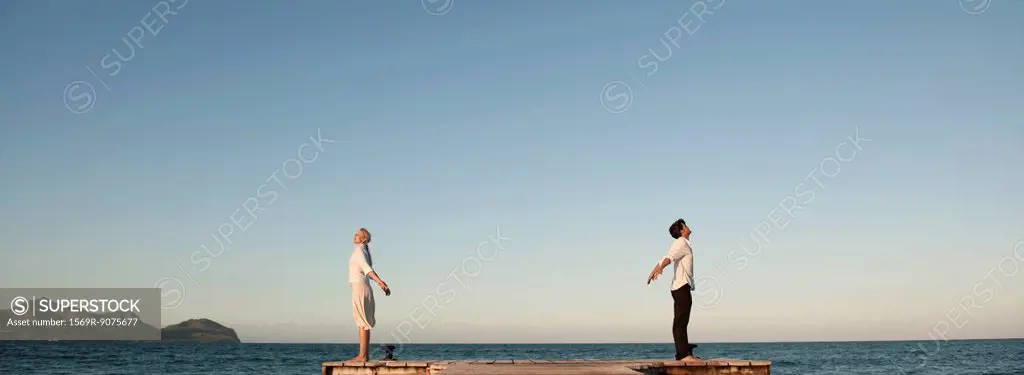 Couple standing back to back on pier, arms out stretched and eyes closed