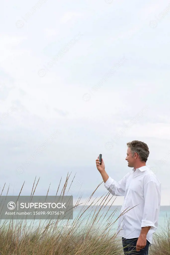 Mature man photographing scenery with cell phone