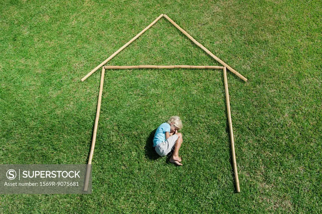 Boy in fetal position within outline of house, high angle view