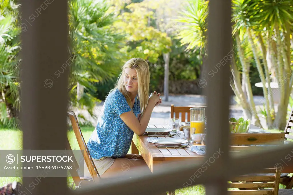 Woman sitting at outdoor table, gazing over shoulder