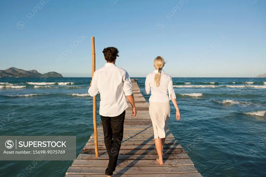 Couple walking on pier over water, rear view