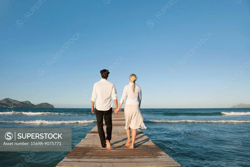 Couple walking on pier holding hands, rear view