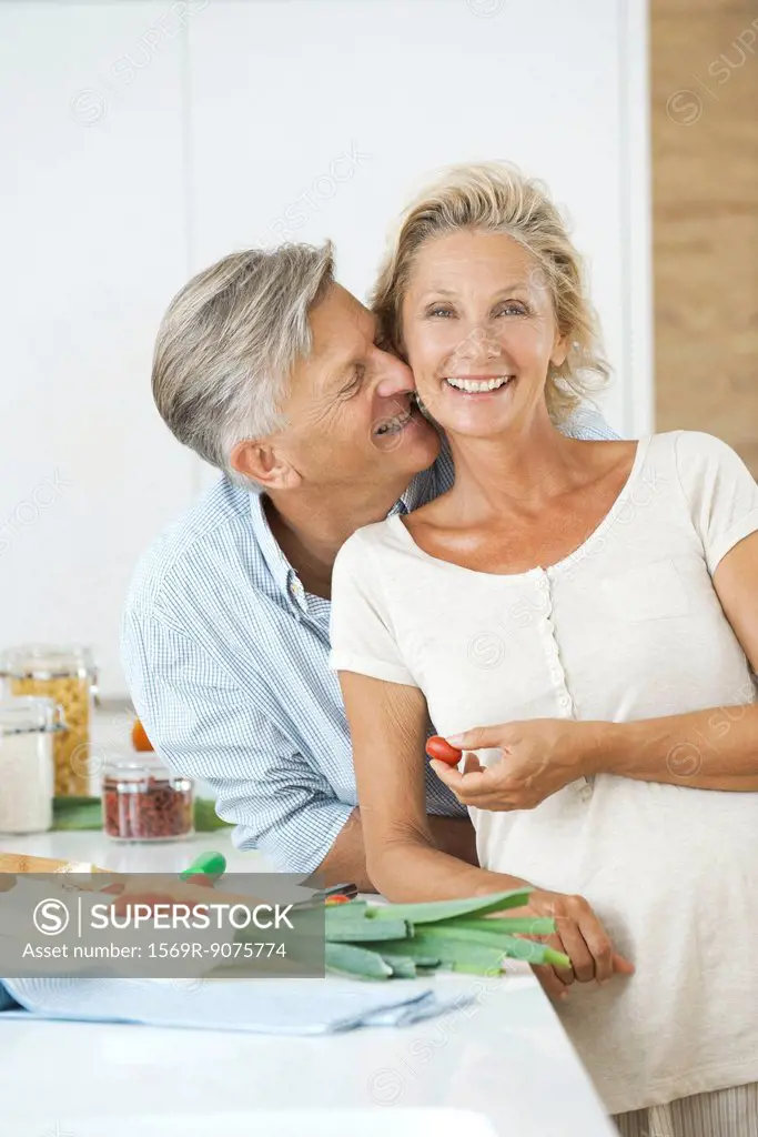 Mature couple together in kitchen, man nuzzling woman, portrait