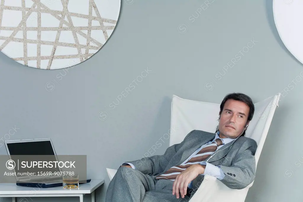 Mature businessman relaxing on chair with earphones