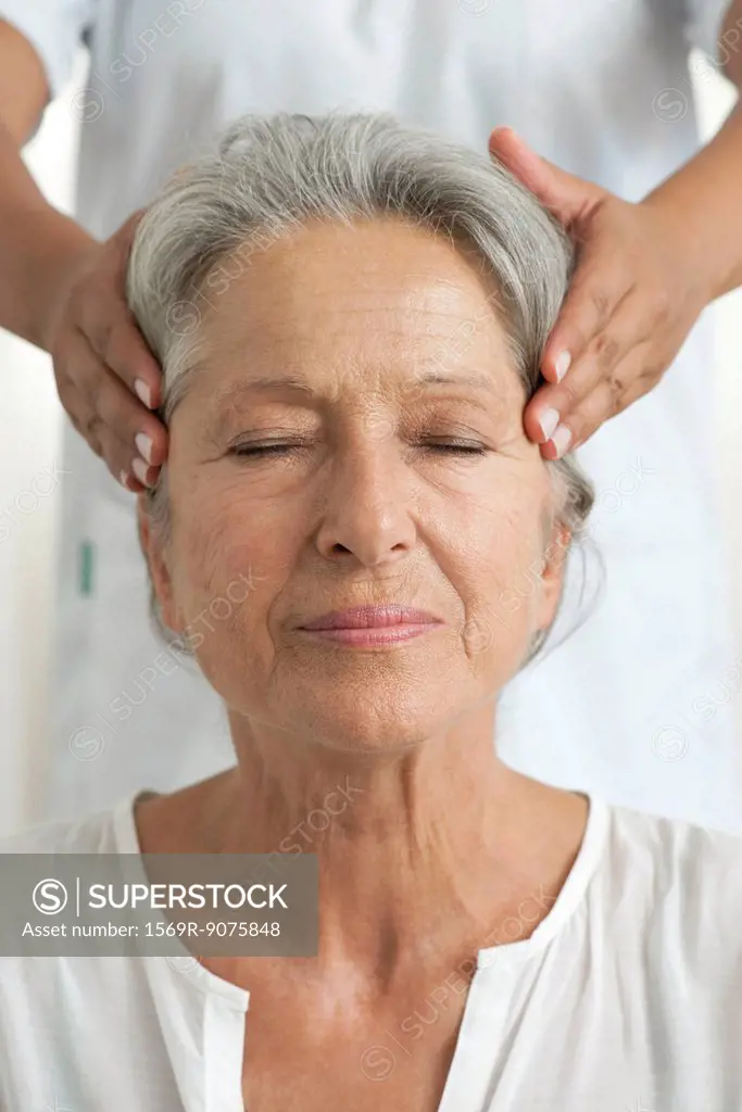 Senior woman having her temples massaged, cropped